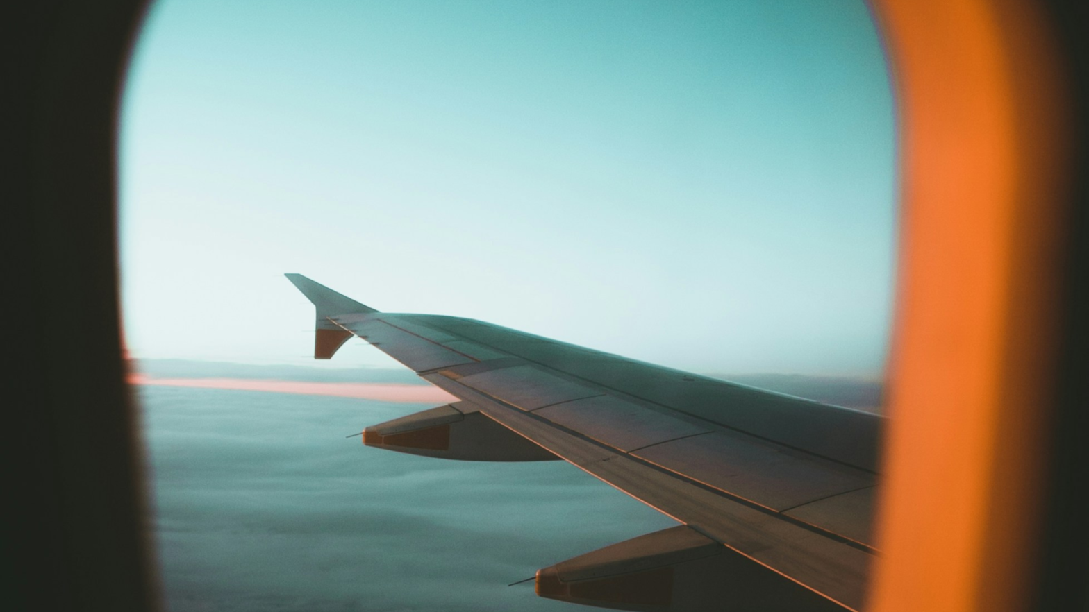 View of an airplane wing from a passenger window, flying above the clouds at sunset with a gradient of blue and orange sky- Direct mail campaign